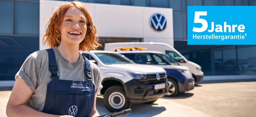 Fröhliche Volkswagen-Mitarbeiterin in Arbeitskleidung vor einem Volkswagen-Nutzfahrzeuge-Gebäude, im Hintergrund mehrere Nutzfahrzeuge, darunter ein weißer Amarok und ein Caddy. Hinweis auf 5 Jahre Herstellergarantie.
