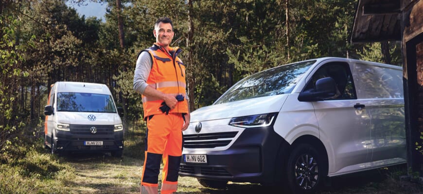 Mann in Warnkleidung steht vor Volkswagen Transporter, im Hintergrund ein Crafter im Wald.