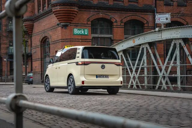 Der Volkswagen ID-Buzz-Taxi fährt über eine Brücke im Stadt-Industriegebiet. Aufgenommen zeigt der Heck das Fahrzeuges.