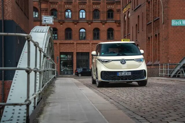 Der Volkswagen ID. Buzz-Taxi fährt über eine Brücke im Stadt-Industriegebiet. Aufgenommen von vorne.