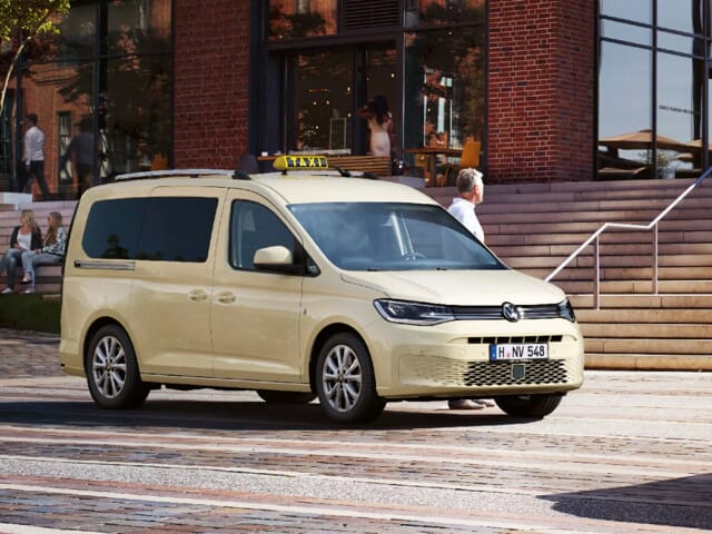 VW-Caddy-Taxi vor einem Backsteingebäude mit Treppen von der Straße zum Eingangsplatz.