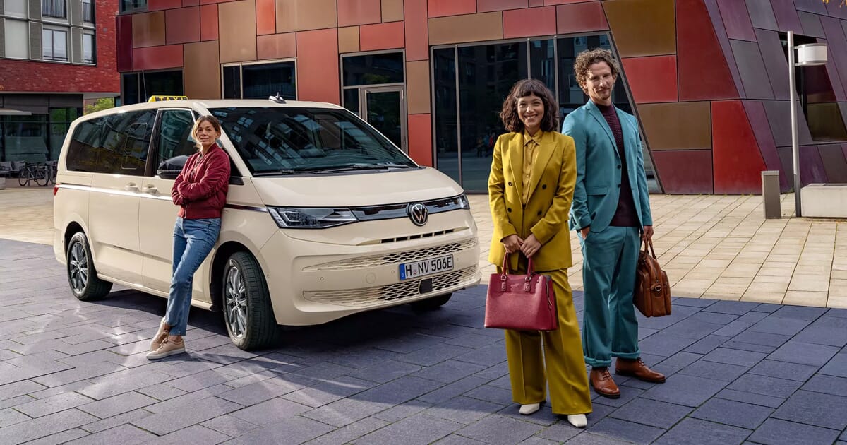 Volkswagen Multivan T7 als Taxi mit Fahrerin und zwei Gästen, die vor dem Taxi posieren.