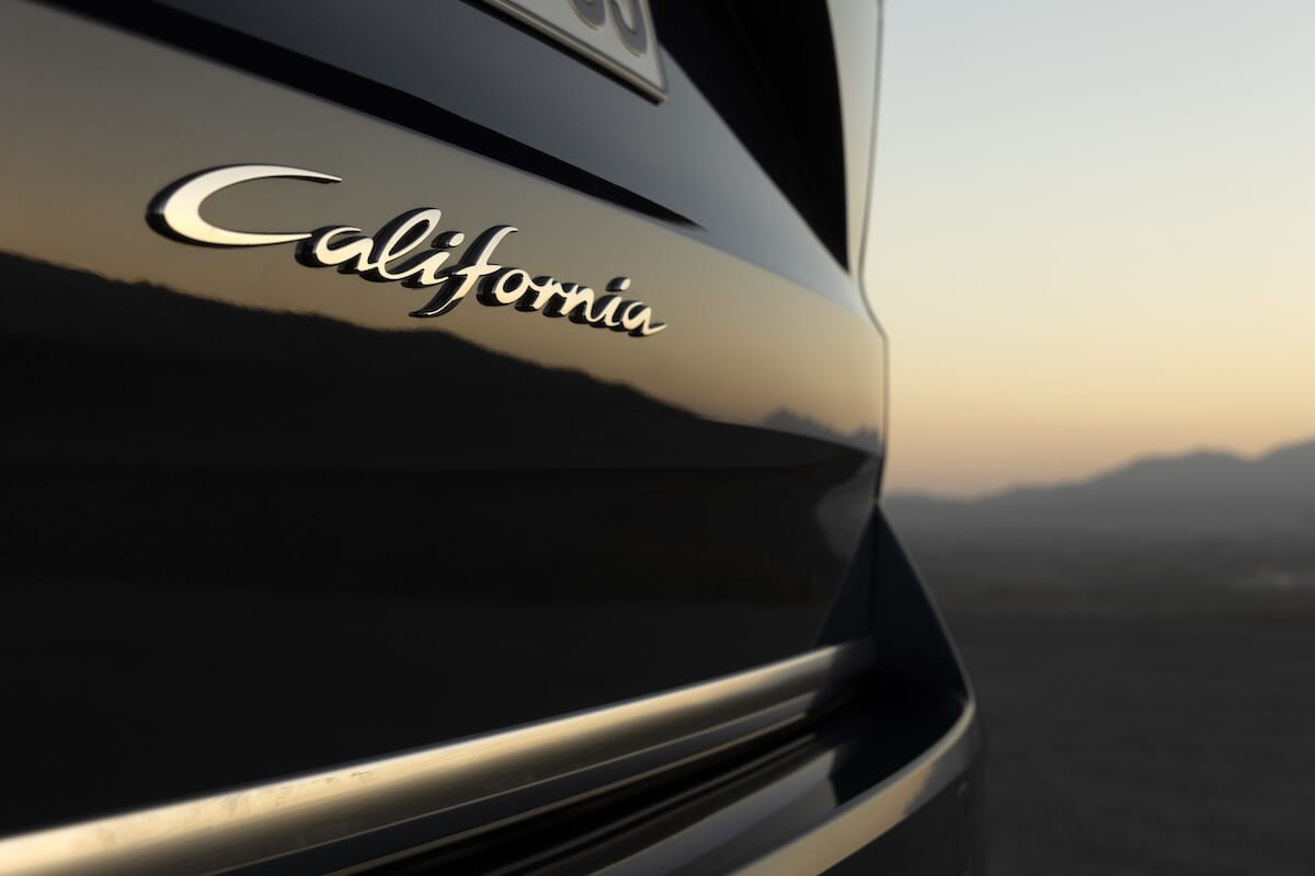Detailansicht des ‘California’-Logos auf dem neuen Volkswagen California mit Sonnenuntergang im Hintergrund.
