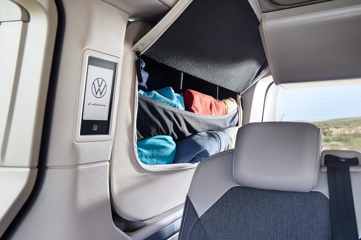 Stauraum im Inneren des neuen Volkswagen California mit ordentlich gefalteter Kleidung und einem Bedienfeld an der Seite.