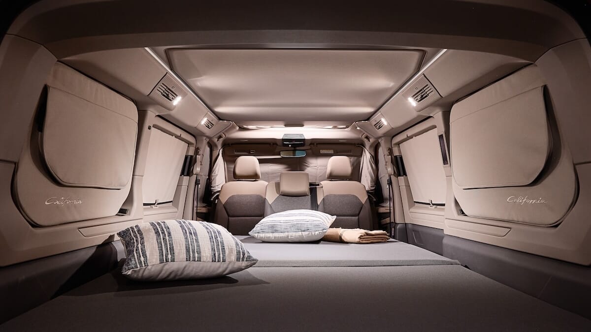 Innenraum des neuen Volkswagen California, konfiguriert zum Schlafen, mit einem Bett, Kissen und gefalteter Decke.
