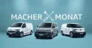 Drei Volkswagen Nutzfahrzeuge vor hellblauer Wand mit Aufschrift 'Macher Monat' und Werkzeug-Symbol: weißer E-Transporter, grauer Transporter und weißer ID. Buzz Cargo mit schwarzem Stoßfänger.