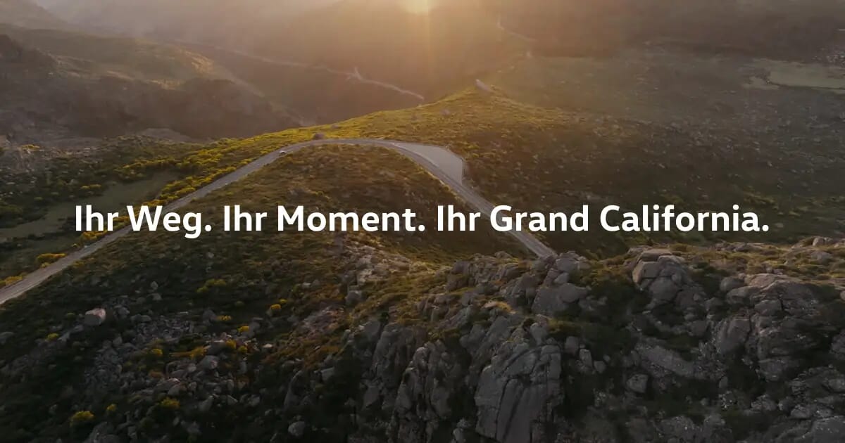 Luftaufnahme einer kurvenreichen Bergstraße bei Sonnenuntergang mit einem Volkswagen Grand California in der Ferne. Text-Overlay: Ihr Weg. Ihr Moment. Ihr Grand California.
